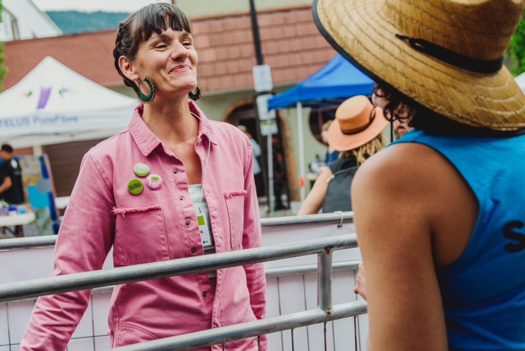Amber Santos at the festival wearing three Nelson International Mural Festival pins on a bright pink shirt.