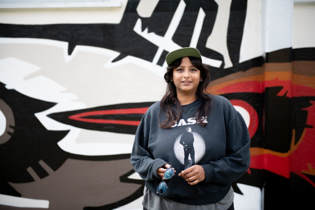 fatspatrol in front of her Lakeside Park mural (a bird and raccoon in bold black lines are visible behind her)